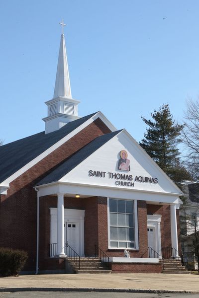 Saint Thomas Aquinas Church, brick building with white steeple and sign, blue sky background.