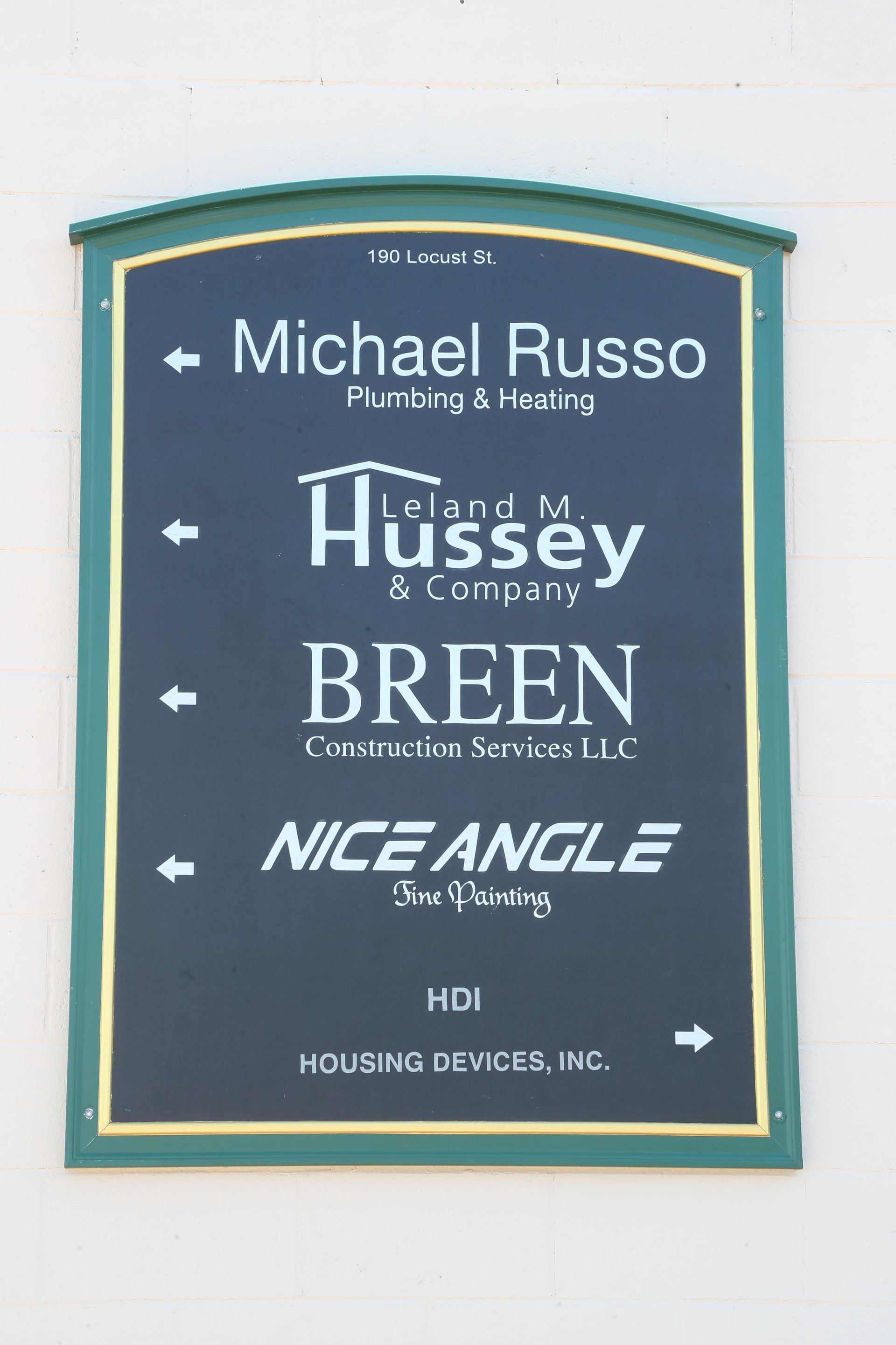 Sign with green border lists businesses: Michael Russo (plumbing), Hussey & Company, Breen, Nice Angle, and Housing Devices, Inc.