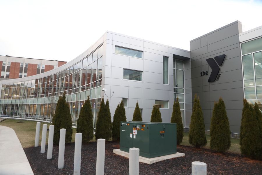 Modern YMCA building with glass windows, silver panels, and a grassy area.