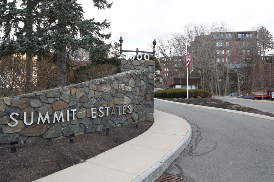 Sign for Summit Estates, stone wall with text, road, and apartment building in the background.