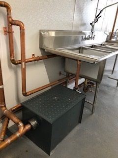Copper pipes and stainless steel sink in a commercial kitchen with a grease trap.