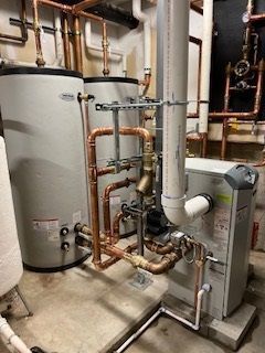 Copper pipes and two silver tanks connected to HVAC equipment in a basement.