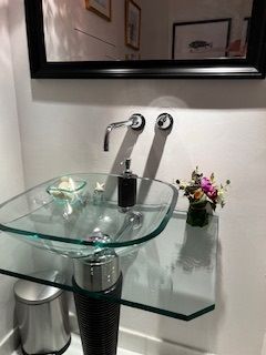 Glass sink with chrome faucet and fixtures, on a glass shelf.
