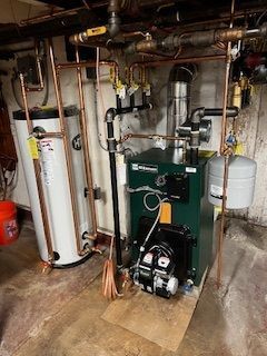 A boiler and water heater with copper pipes in a basement setting.