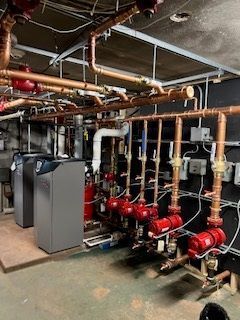 Complex plumbing system with copper pipes and red pumps in a basement setting.