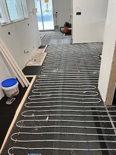 Radiant floor heating system installation: tubing laid on black matting in a room under construction.