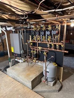 Copper pipes and mechanical components on a basement wall. Gray tank and a concrete base are visible.