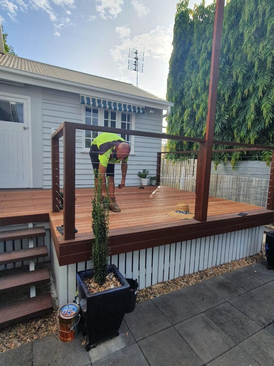 A Man is Working on a Wooden Deck in Front of a House — Wilkinson Homes in Annandale, QLD