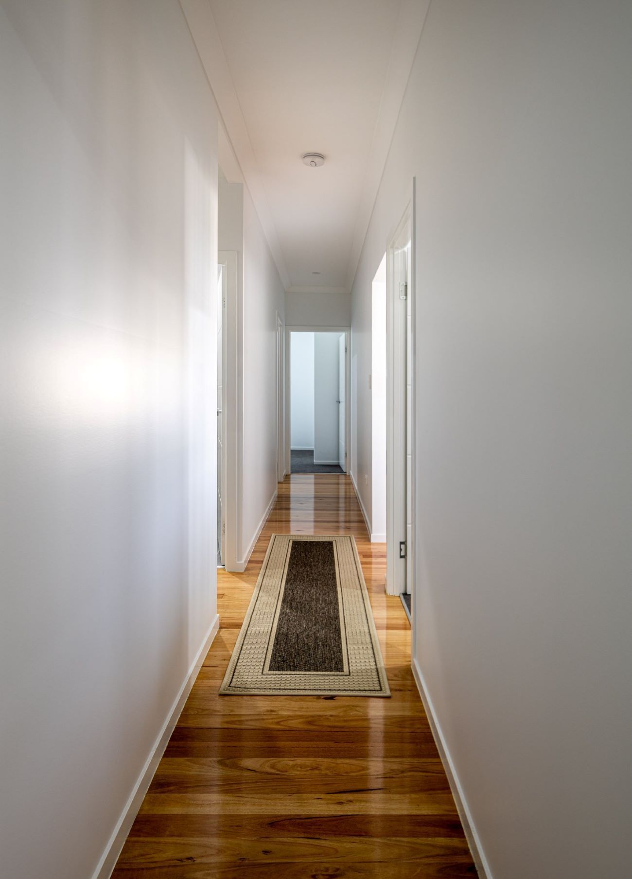 A Long Hallway With a Rug on the Floor and White Walls — Wilkinson Homes in Annandale, QLD