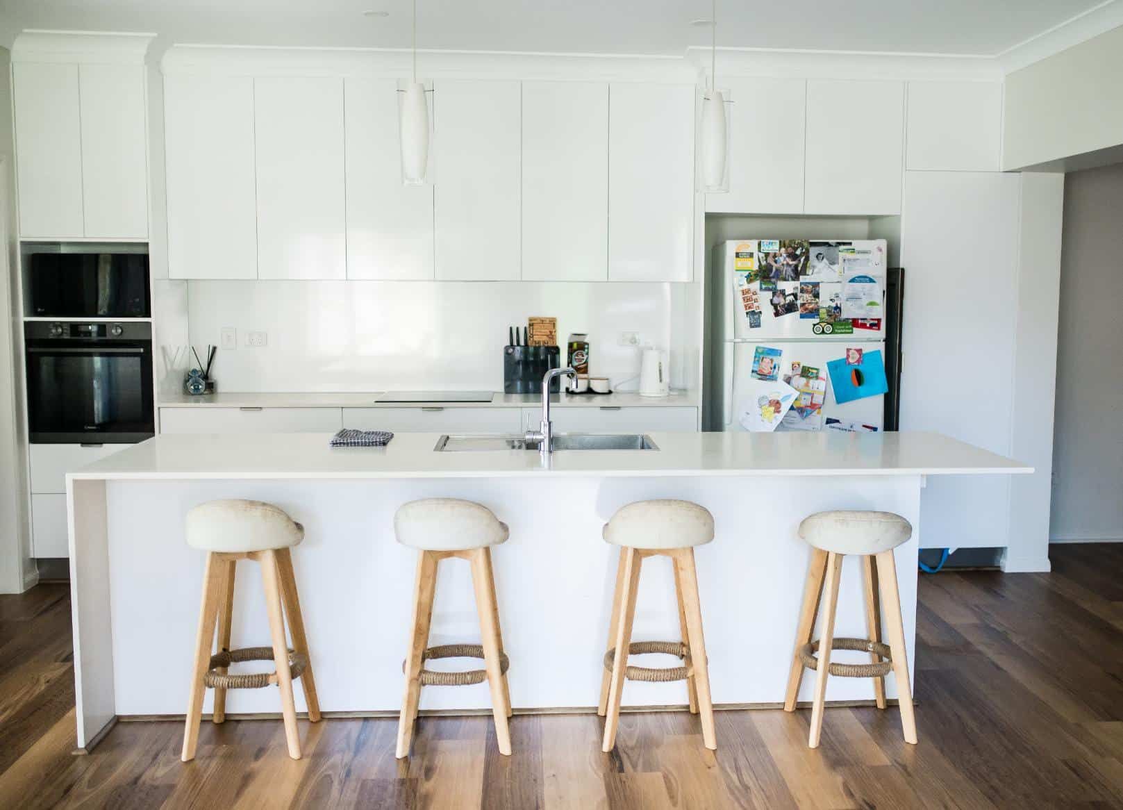 A Kitchen With White Cabinets and Stools and a Refrigerator — Wilkinson Homes in Annandale, QLD