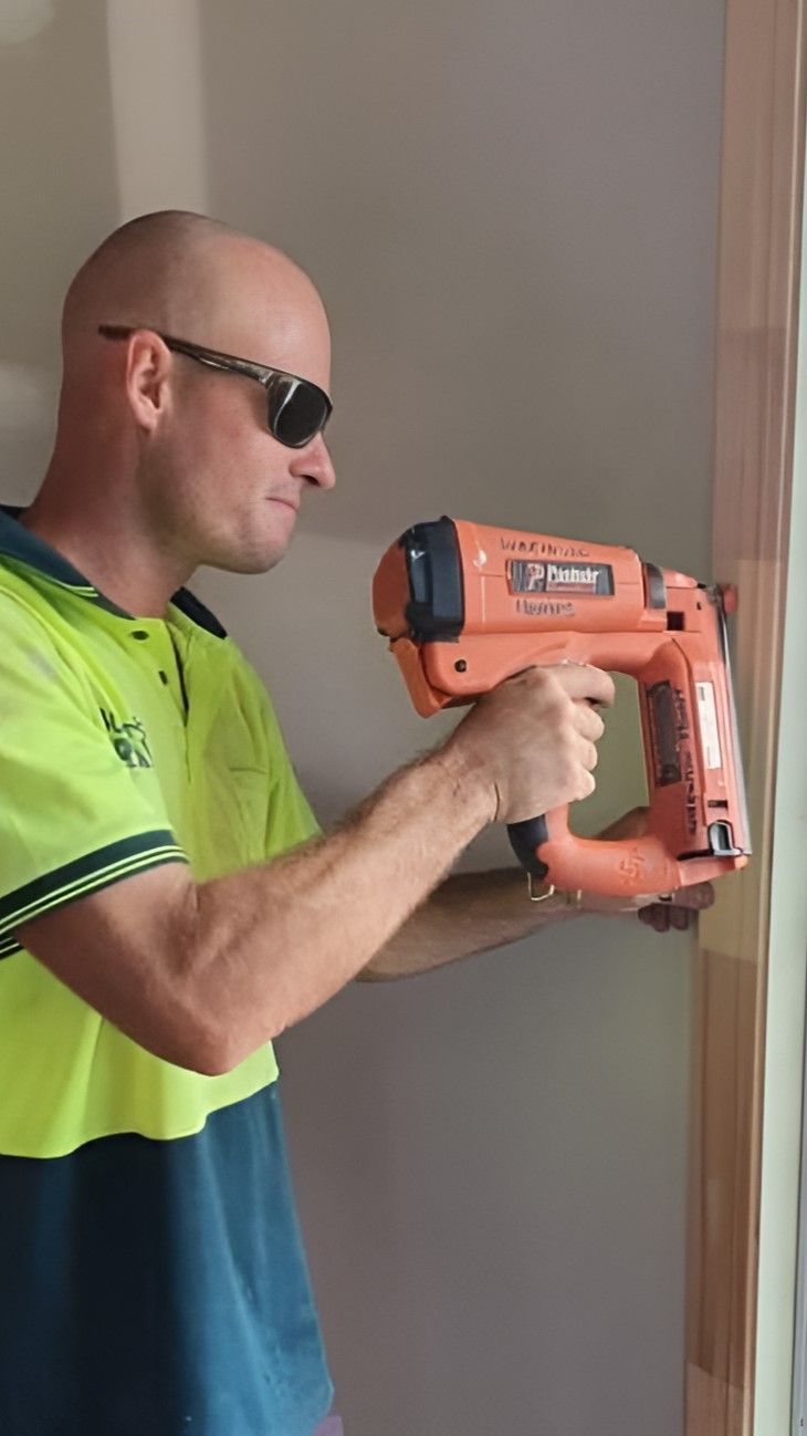 A Man Wearing Sunglasses is Operating a Nail Gun — Wilkinson Homes in Annandale, QLD
