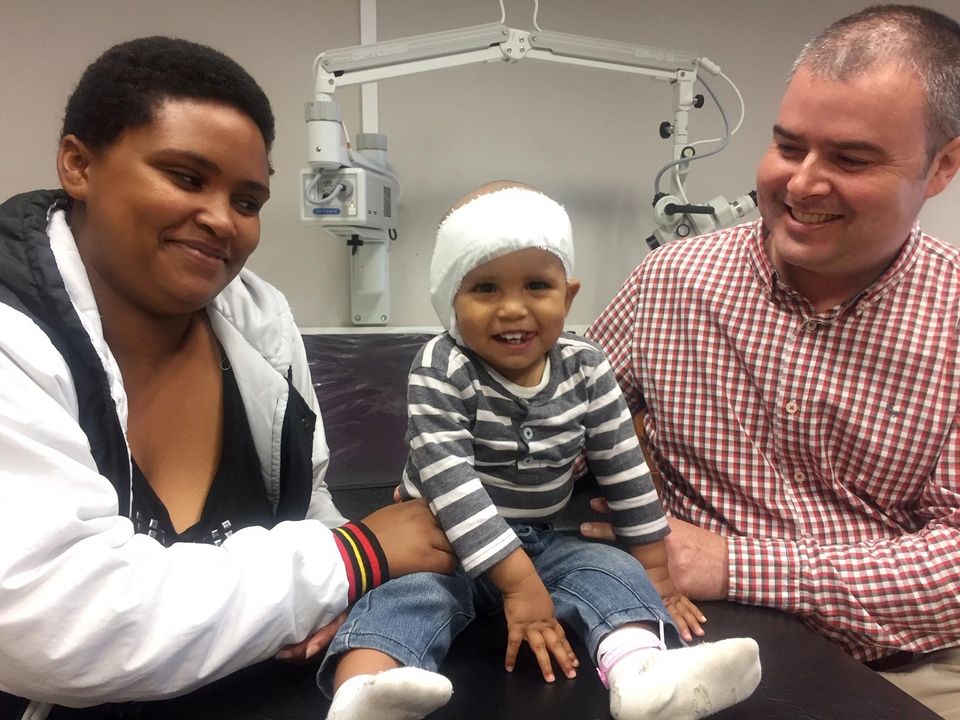 Brave 18-month-old Grayson Marais from Port Elizabeth (centre) pictured just prior to his bandages being removed at  Netcare Greenacres Hospital. With Grayson is his mother Antoinette Marais (left), and Dr Iain Butler, the ear, nose and throat (ENT) specialist who performed the cochlear implant.