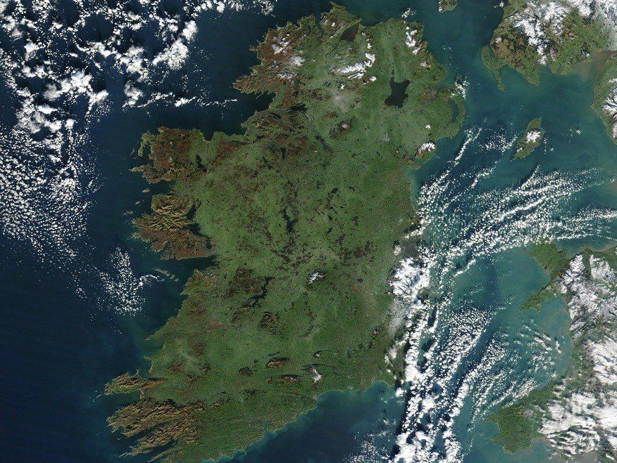 Satellite view of Ireland, mostly green landmass surrounded by blue ocean and white clouds.