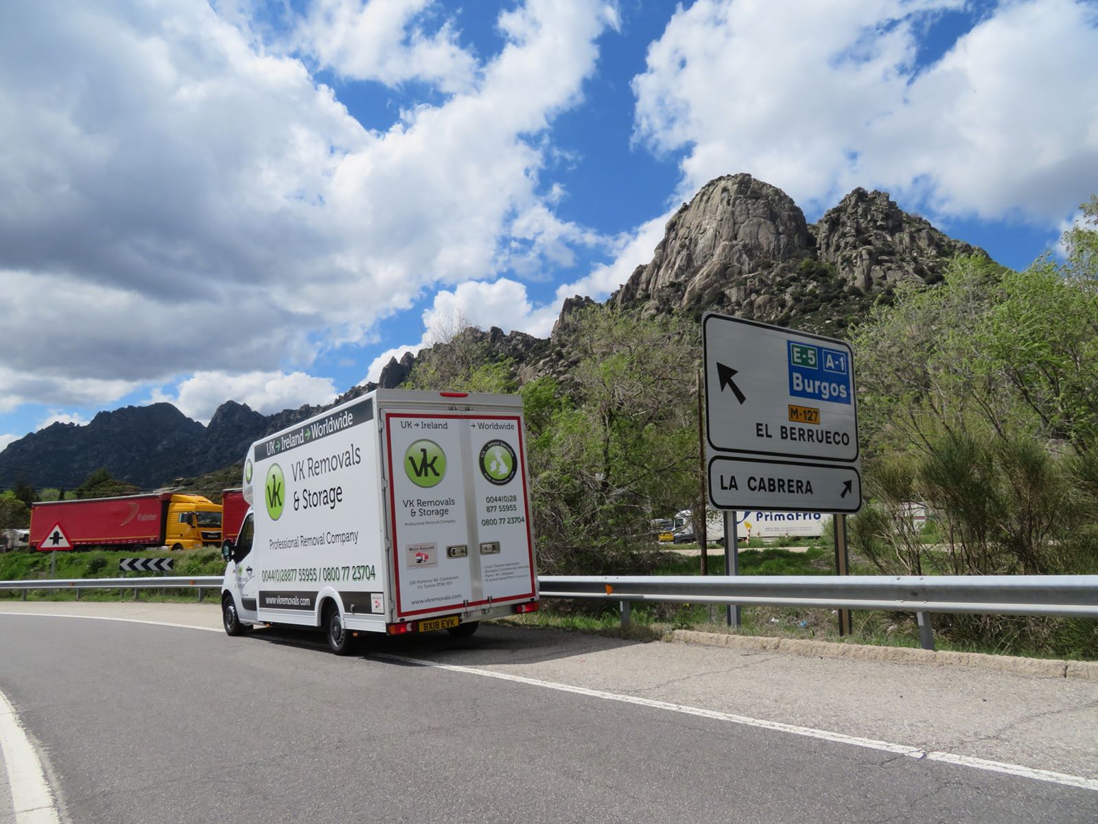 White van parked on a roadside with sign to towns. Mountain in background. Cloudy sky.