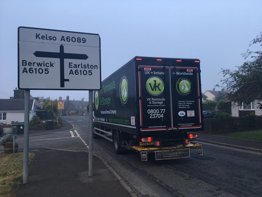Signpost pointing to Kelso, Berwick, and Earlston, with a black truck driving on the road.