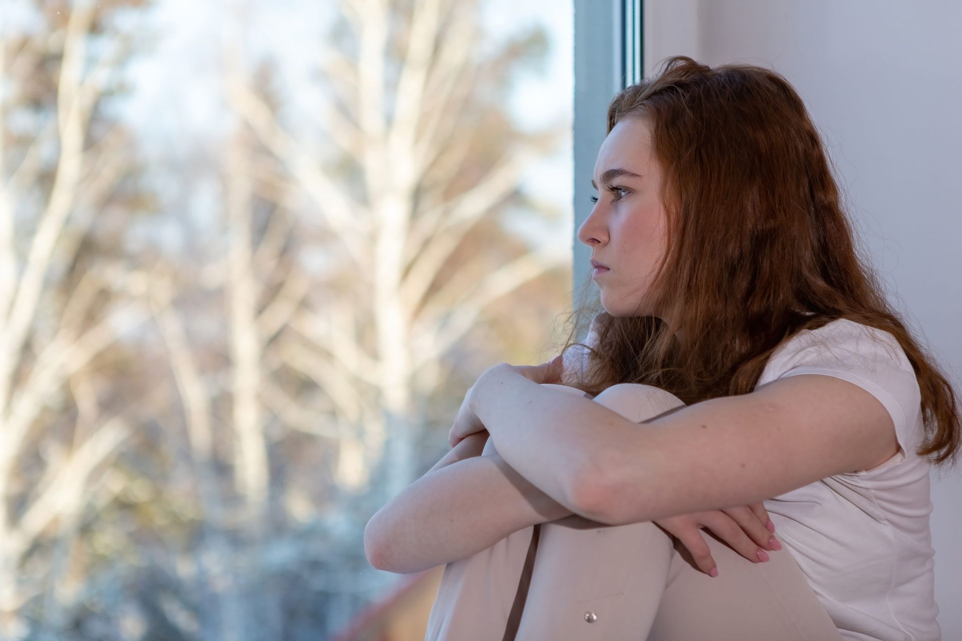 A teen girl looking out a window thoughtfully, teen anxiety therapy in Fairfax VA with Lisa Kelleher