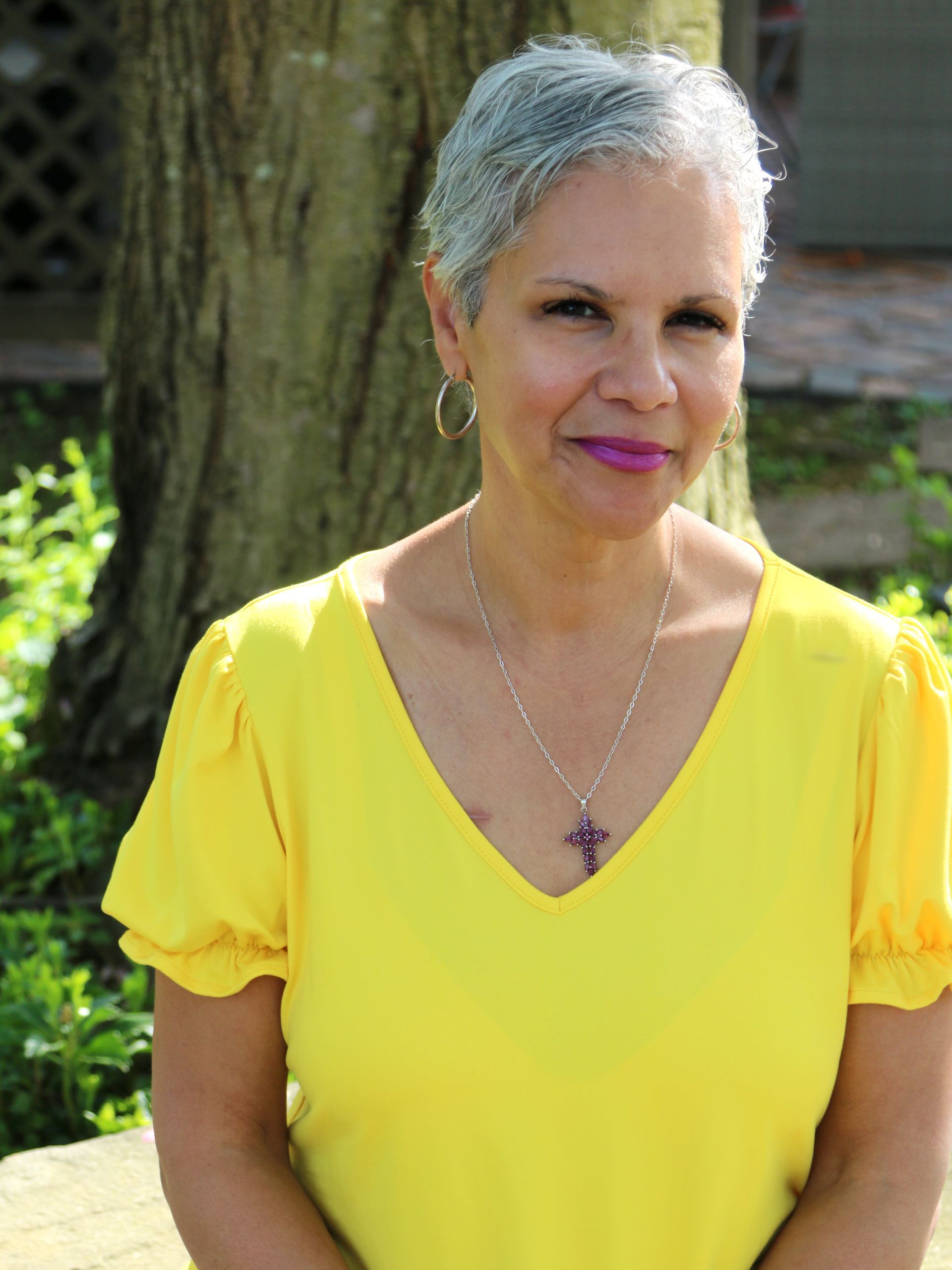 Woman with short gray hair wearing a yellow blouse smiles outdoors.