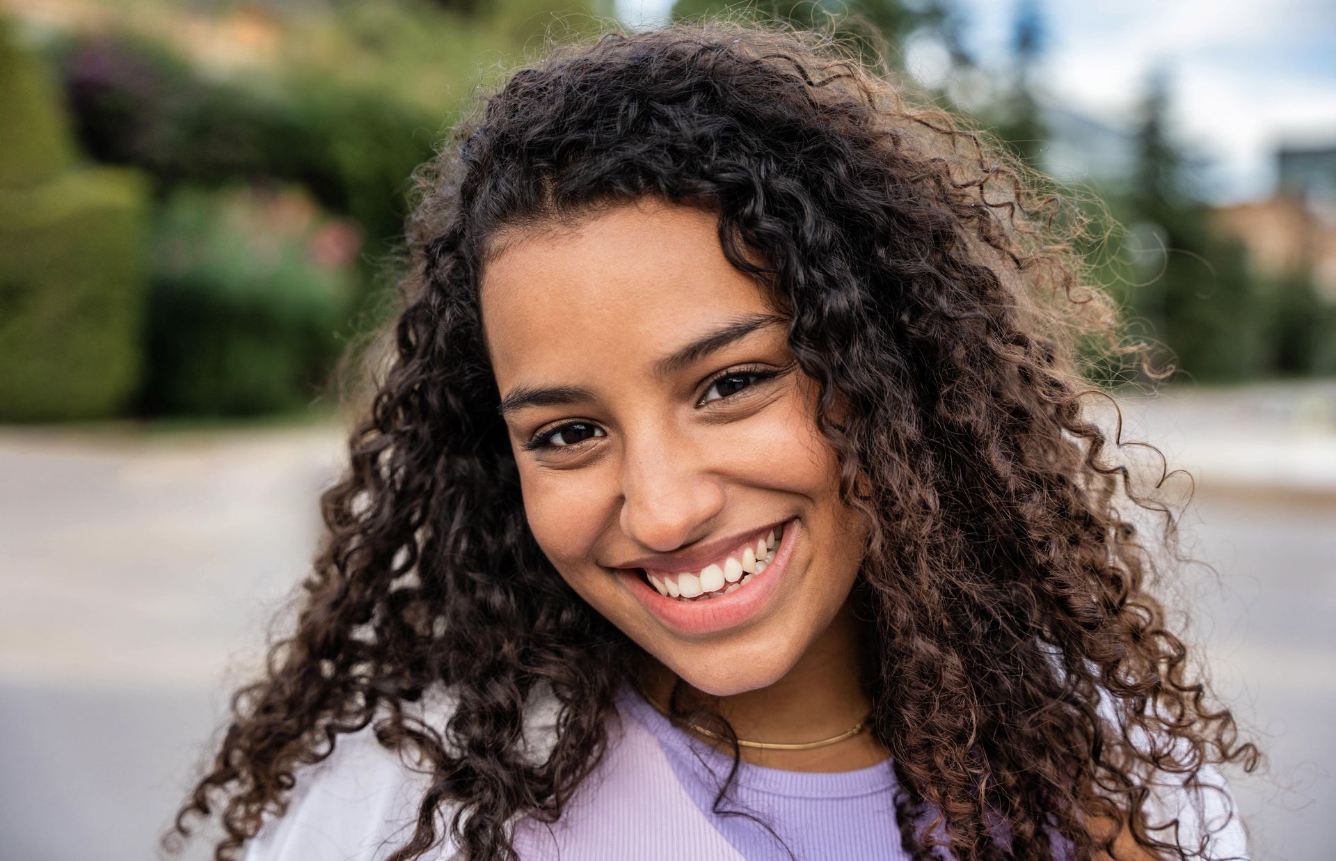 Young woman with curly hair smiles, outside.