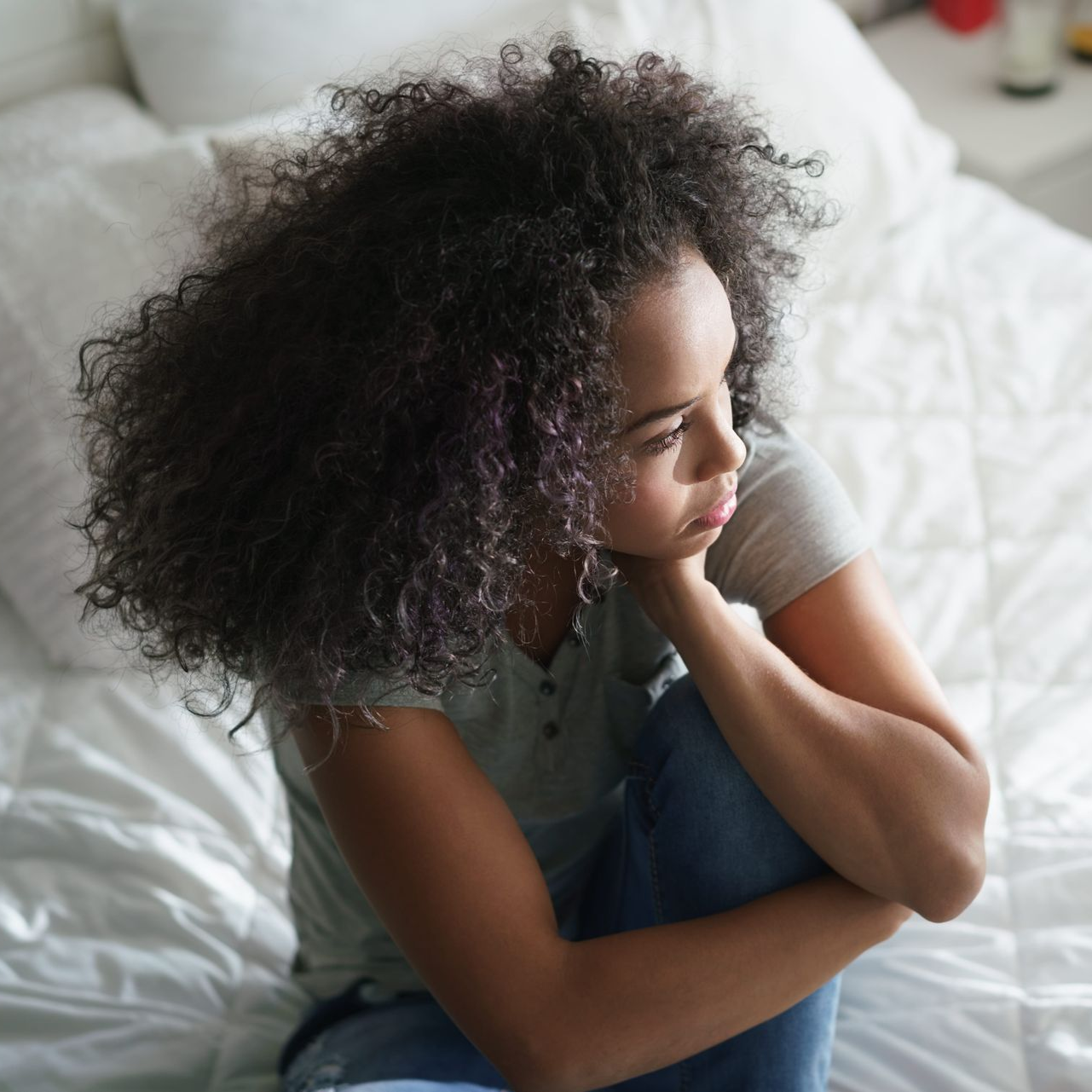 A woman is sitting on a bed with her head down