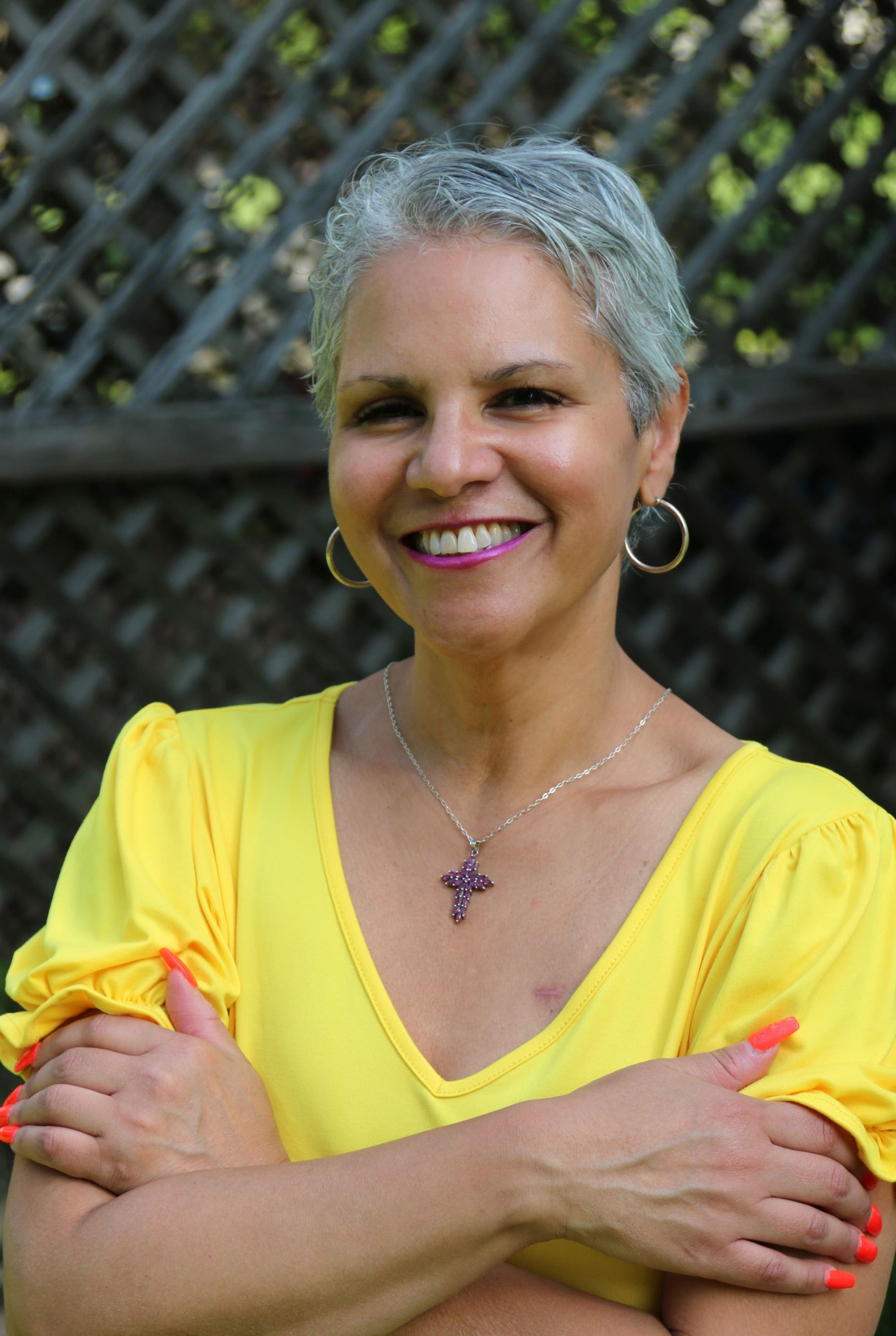 Woman with short gray hair wearing a yellow blouse smiles outdoors.