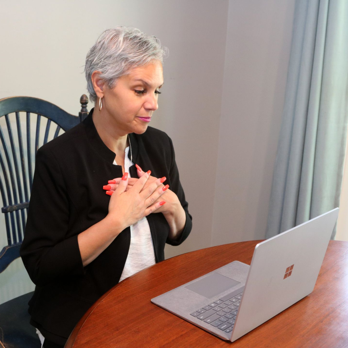 Woman with hands on chest looking at a laptop on a table. She has short gray hair.