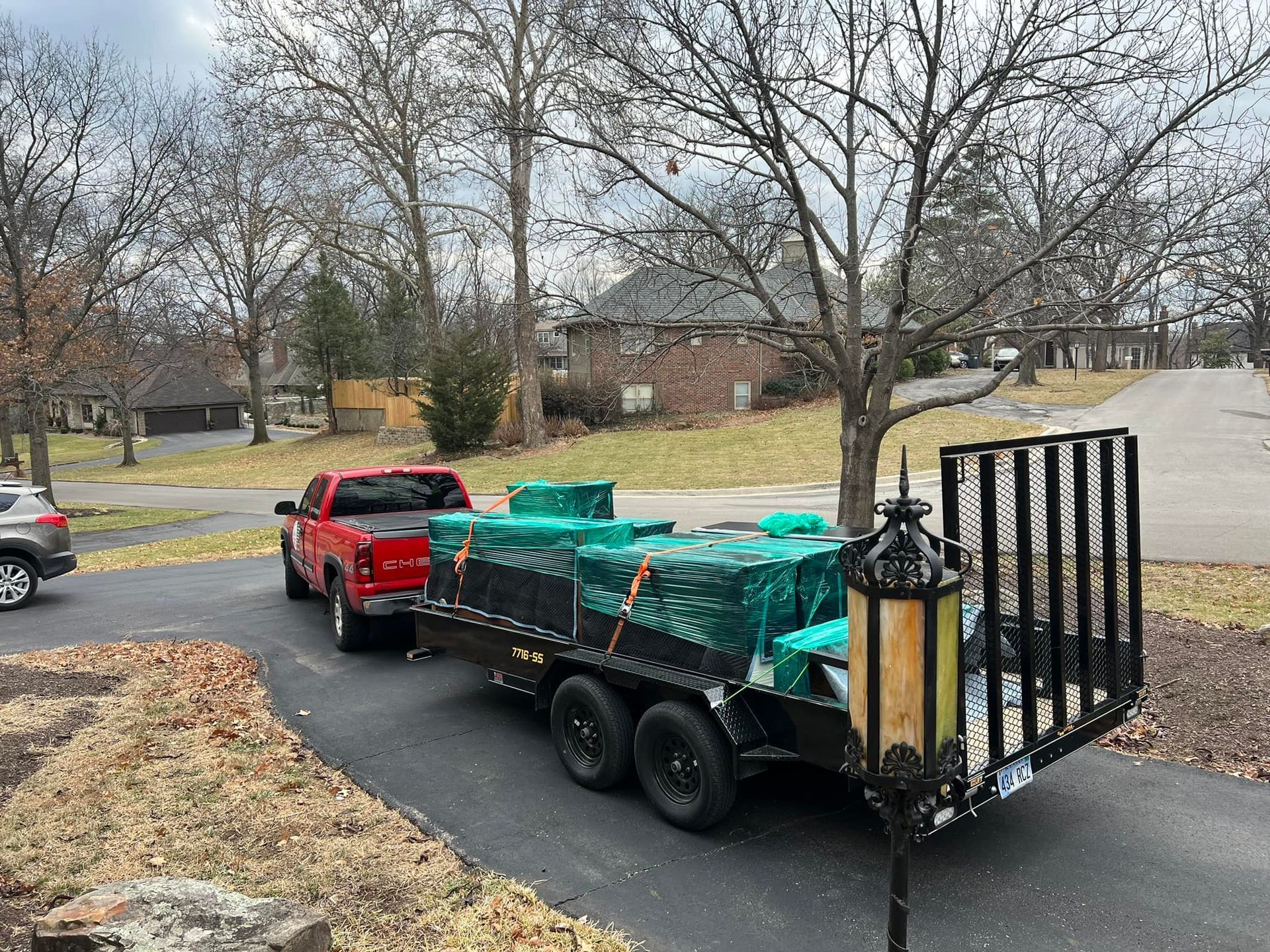 Red pickup truck towing a trailer loaded with covered items on a residential street.