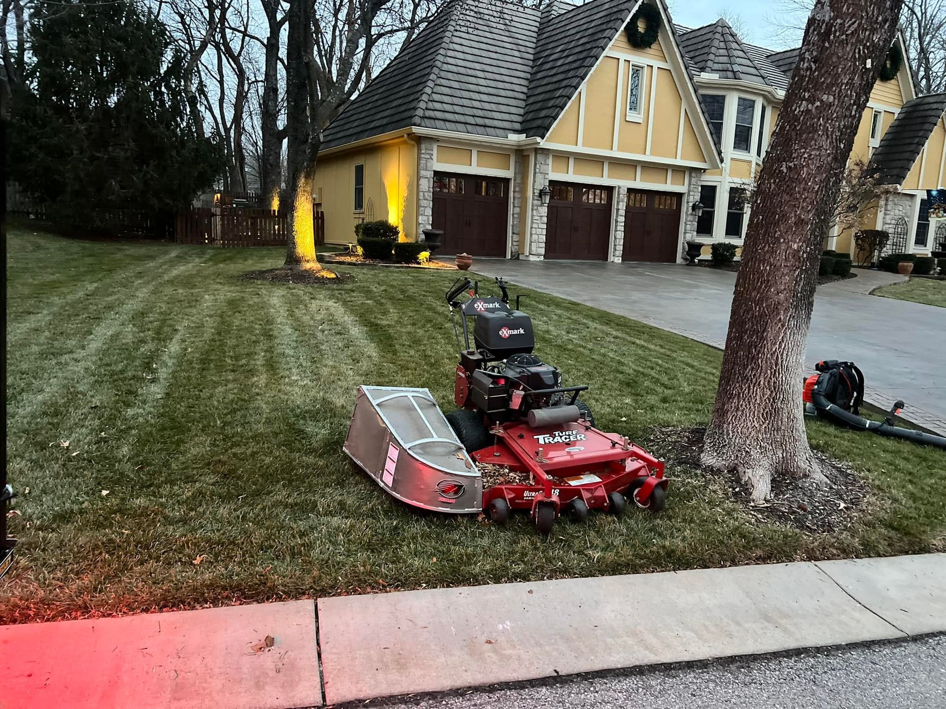 Lawnmower on a sloped yard, near a house with garage, leaves on the ground.