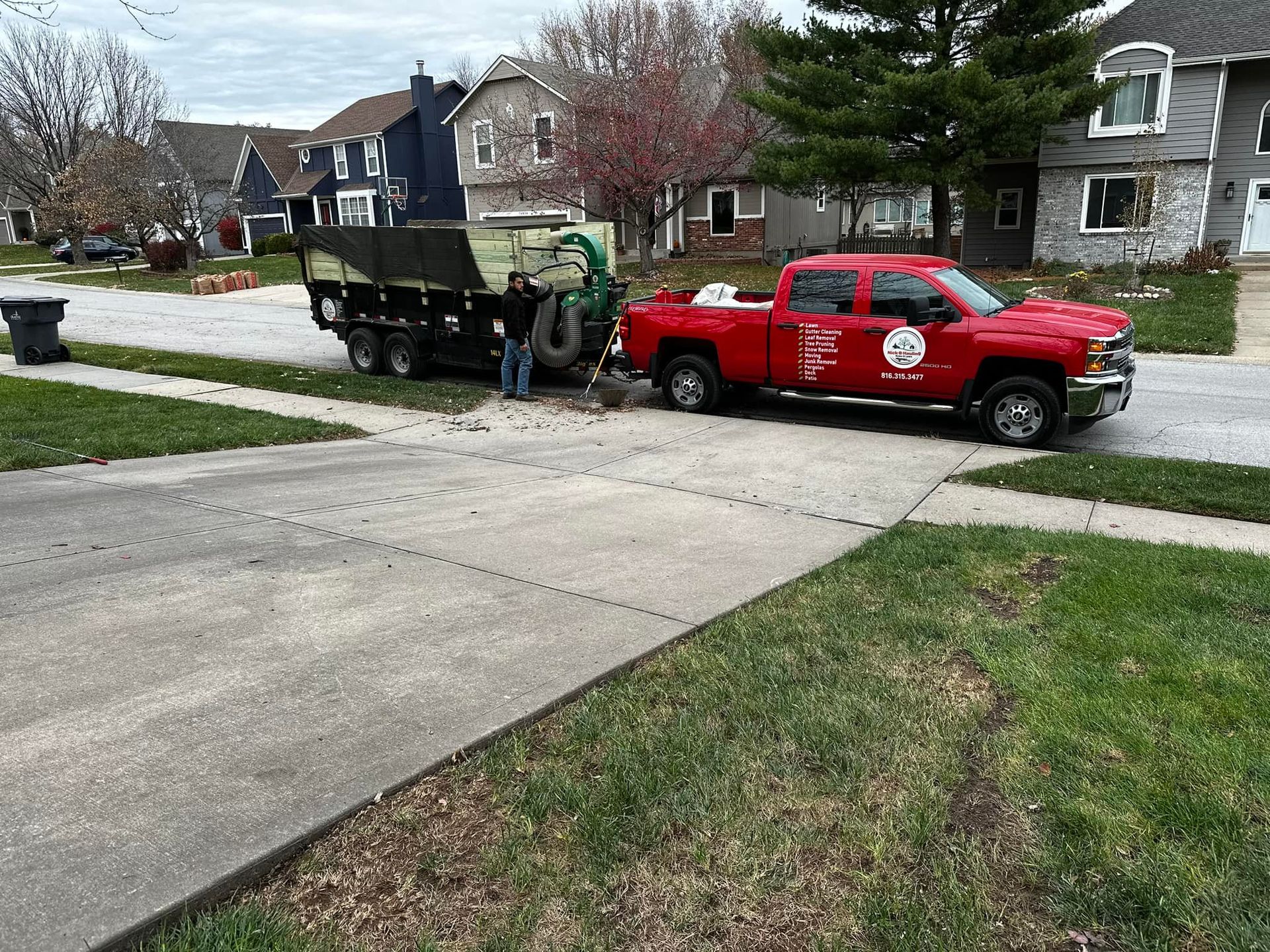 Red pickup truck towing a trailer with a man nearby, in a residential area.