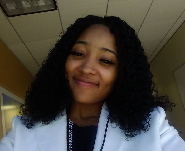 Woman with dark curly hair smiles while wearing a white blazer and black top.