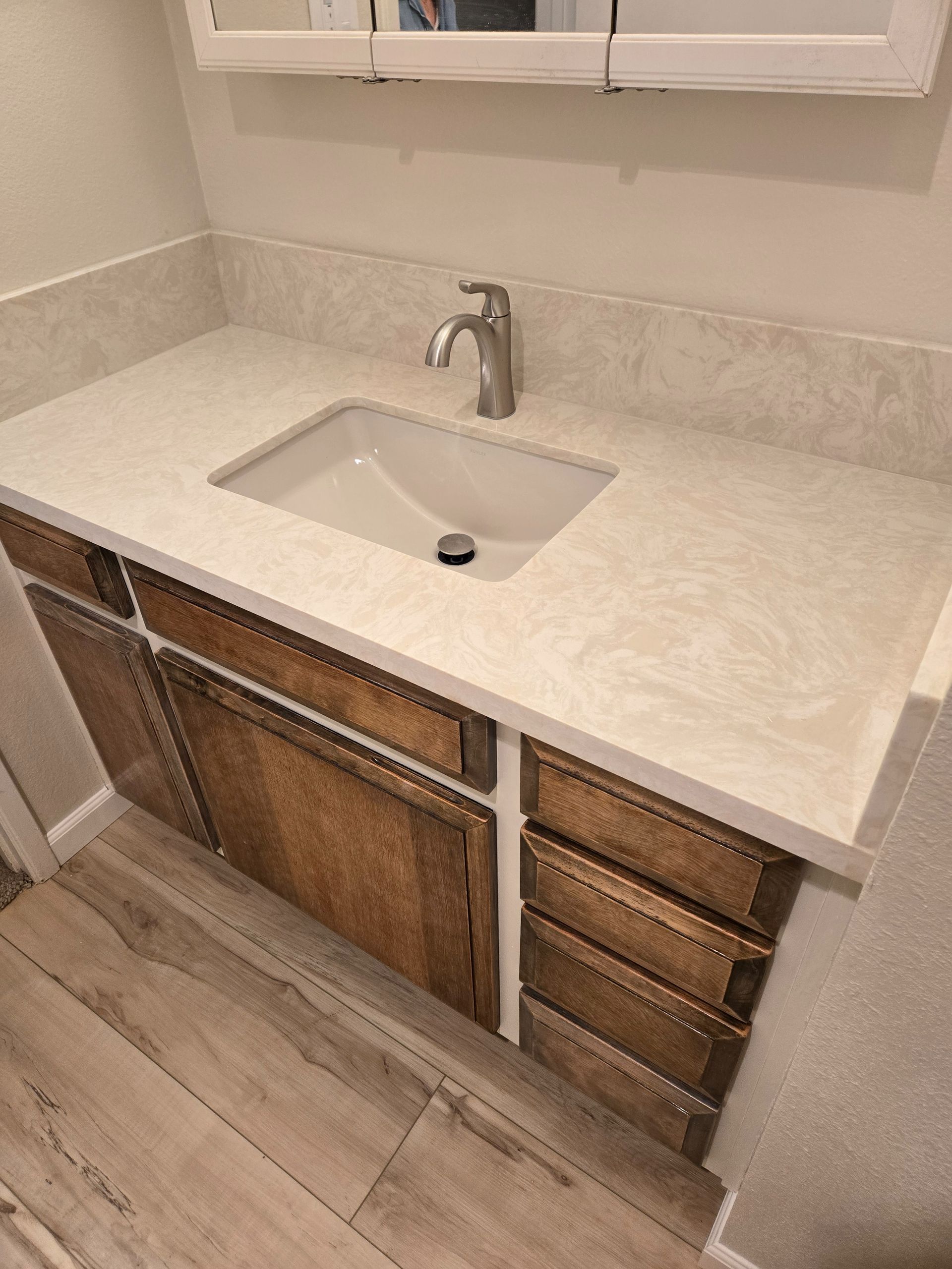 Bathroom vanity with light countertop, white sink, and wood-tone cabinets.
