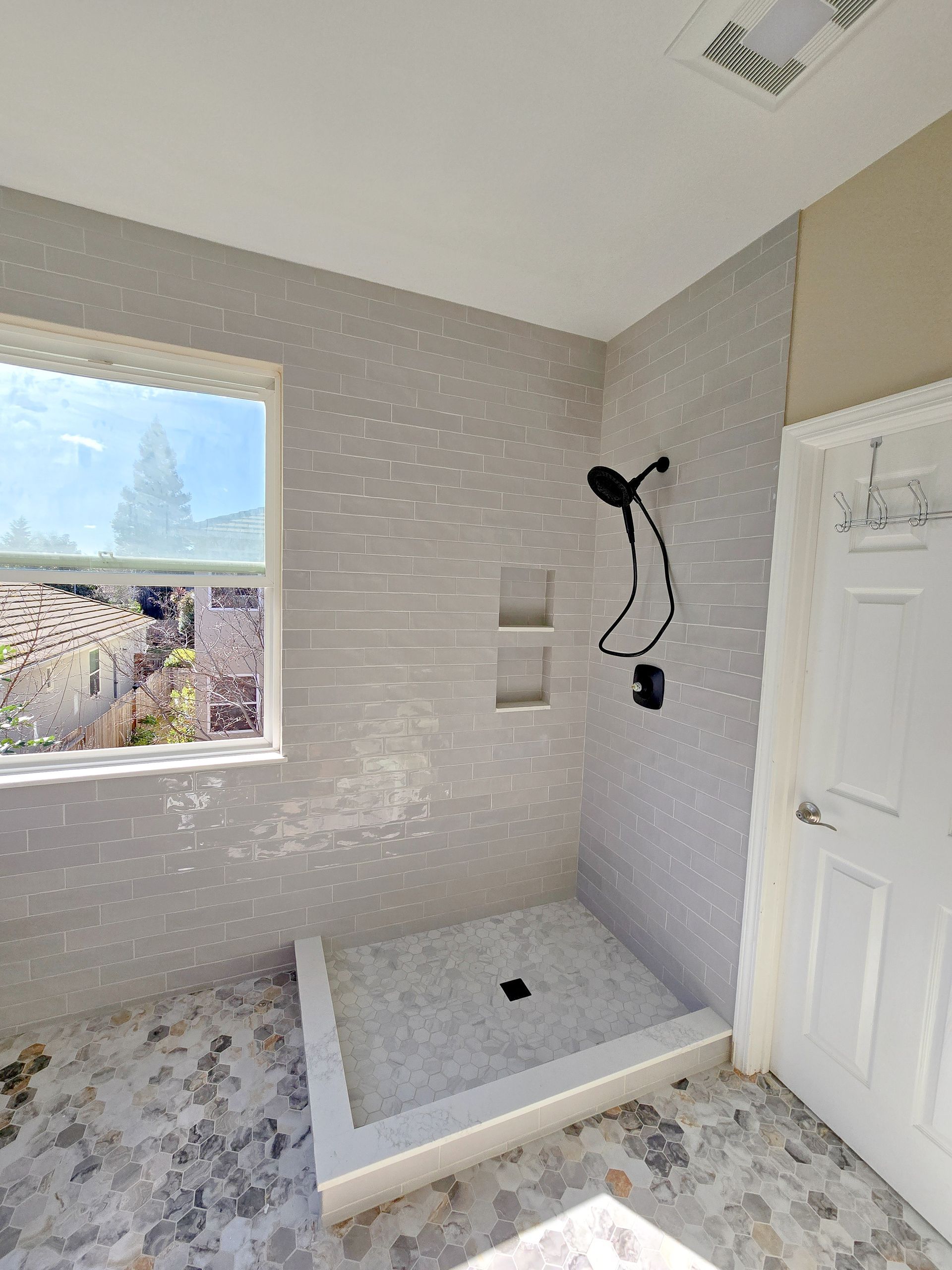 Modern shower with light gray tile walls, window, and black shower head.