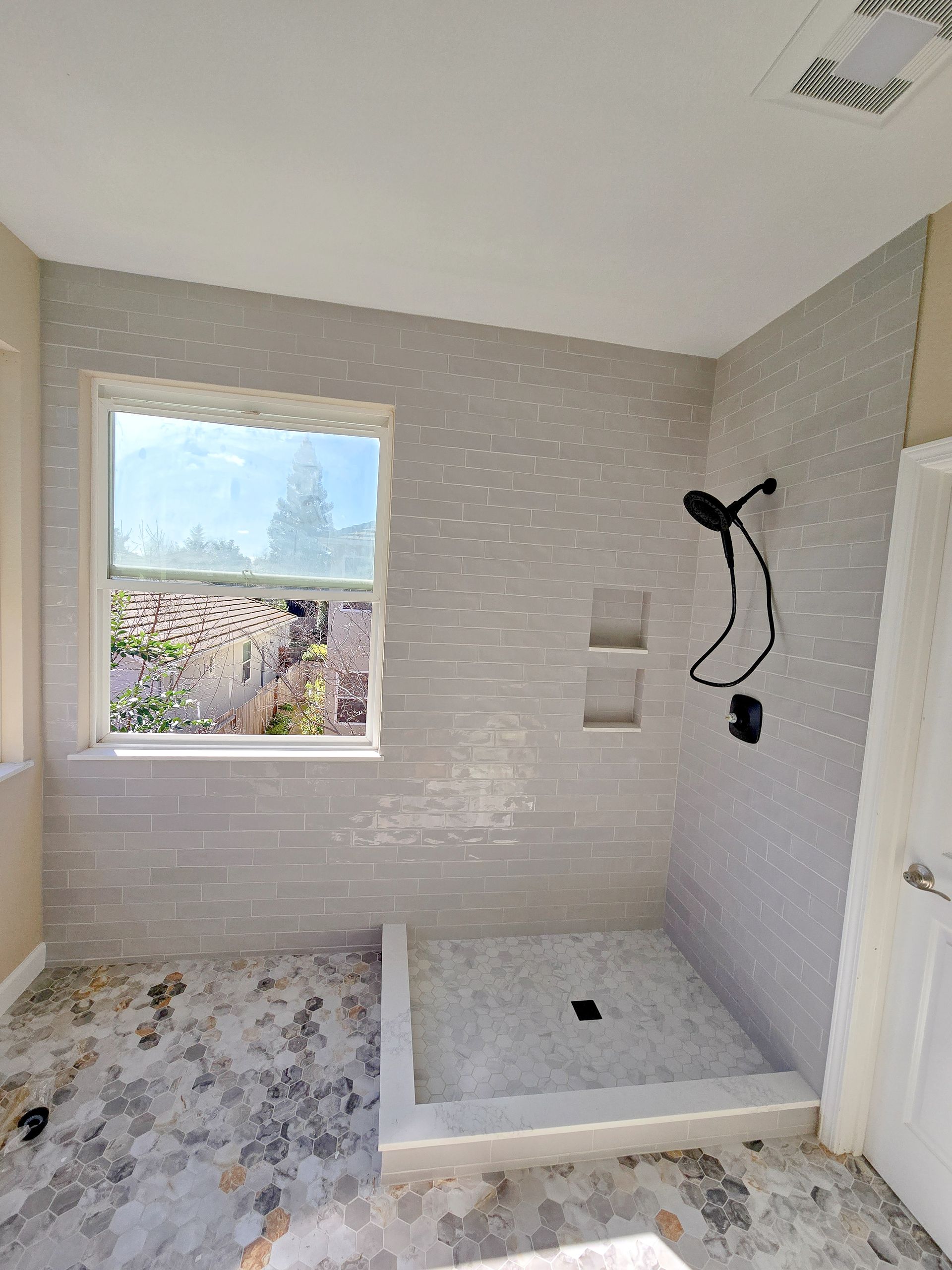 Bathroom with tiled walls, shower, and window. Gray and white color scheme.