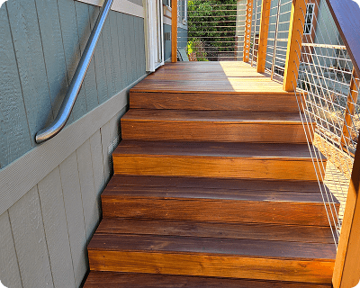 Wooden steps leading up to a doorway, with a metal handrail and wire railings.