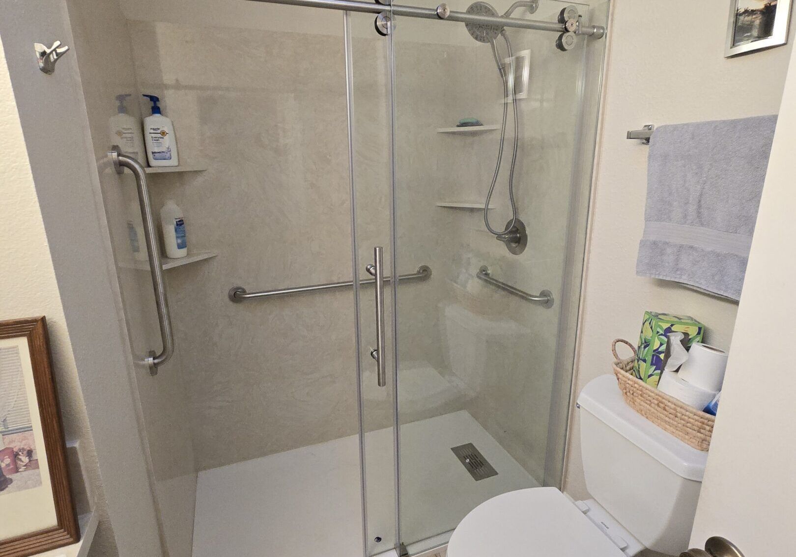 A small bathroom with a glass shower, toilet, towel rack, and decorative items.