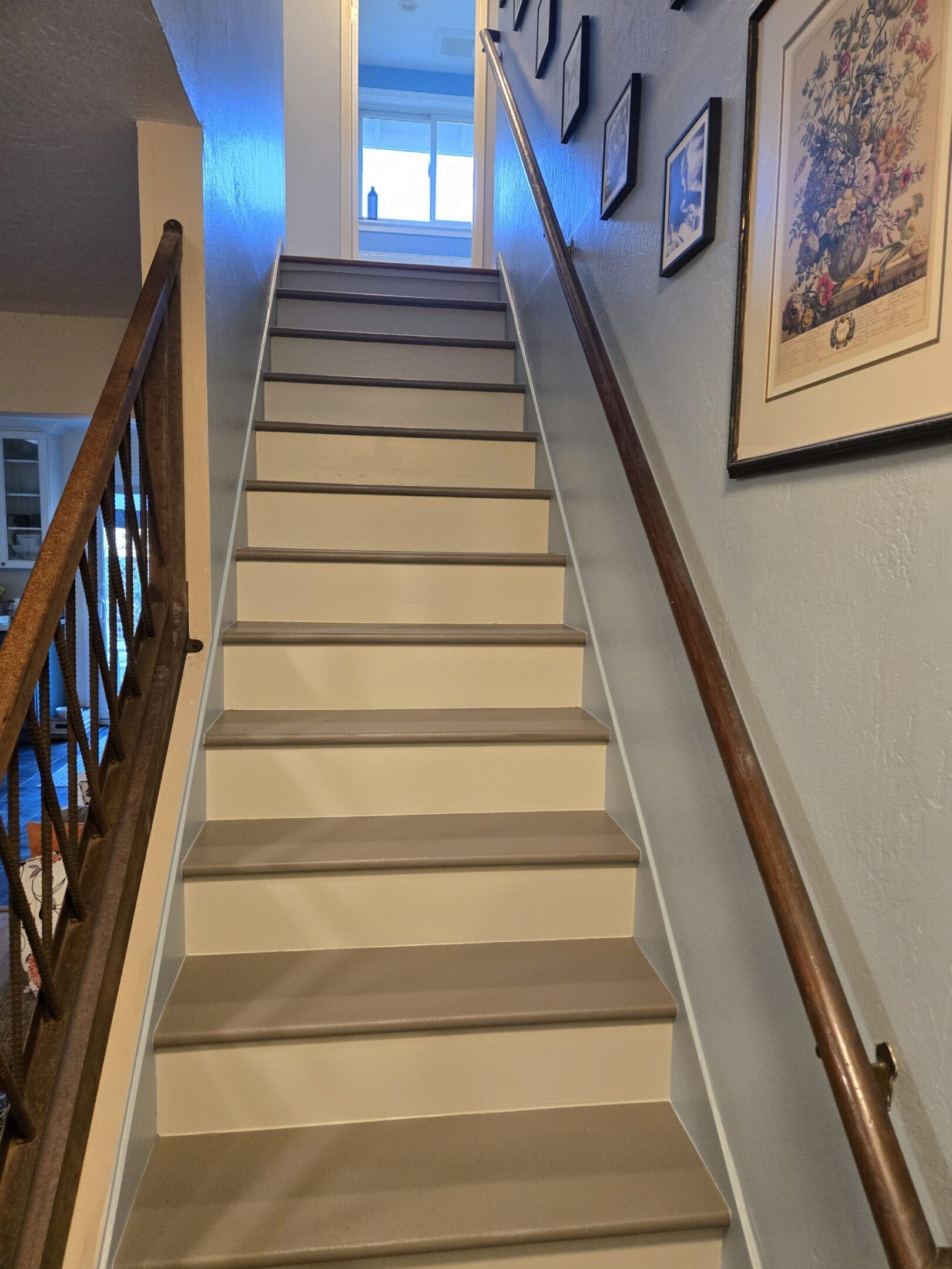 Staircase with light-colored steps, wooden handrails, and a hallway at the top, leading upwards.