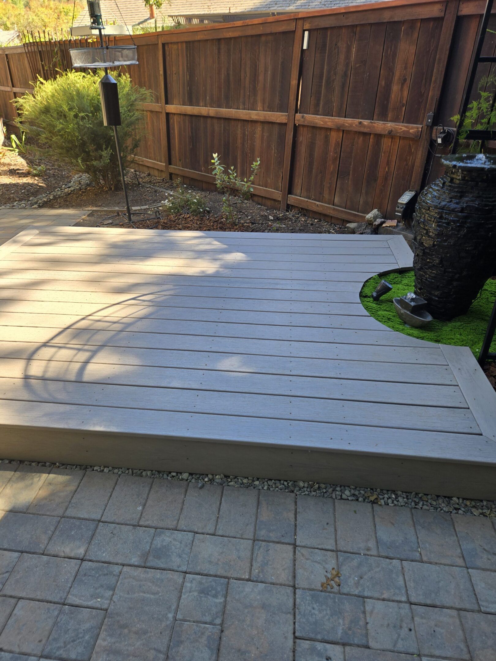 A concrete patio with a curved edge, adjacent to a brick patio and a wooden fence.