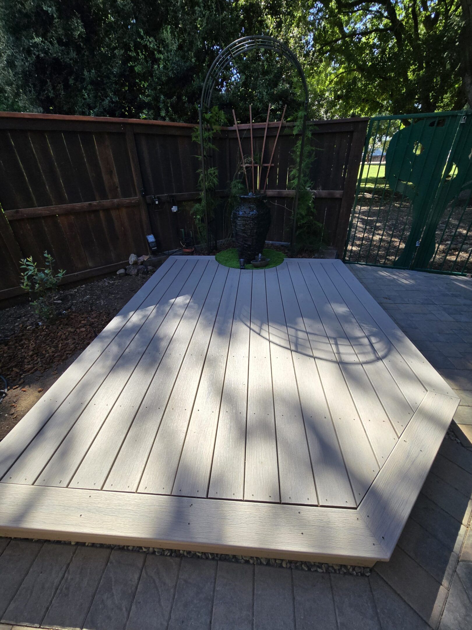 Wooden deck with arched trellis and stone patio in a backyard setting.