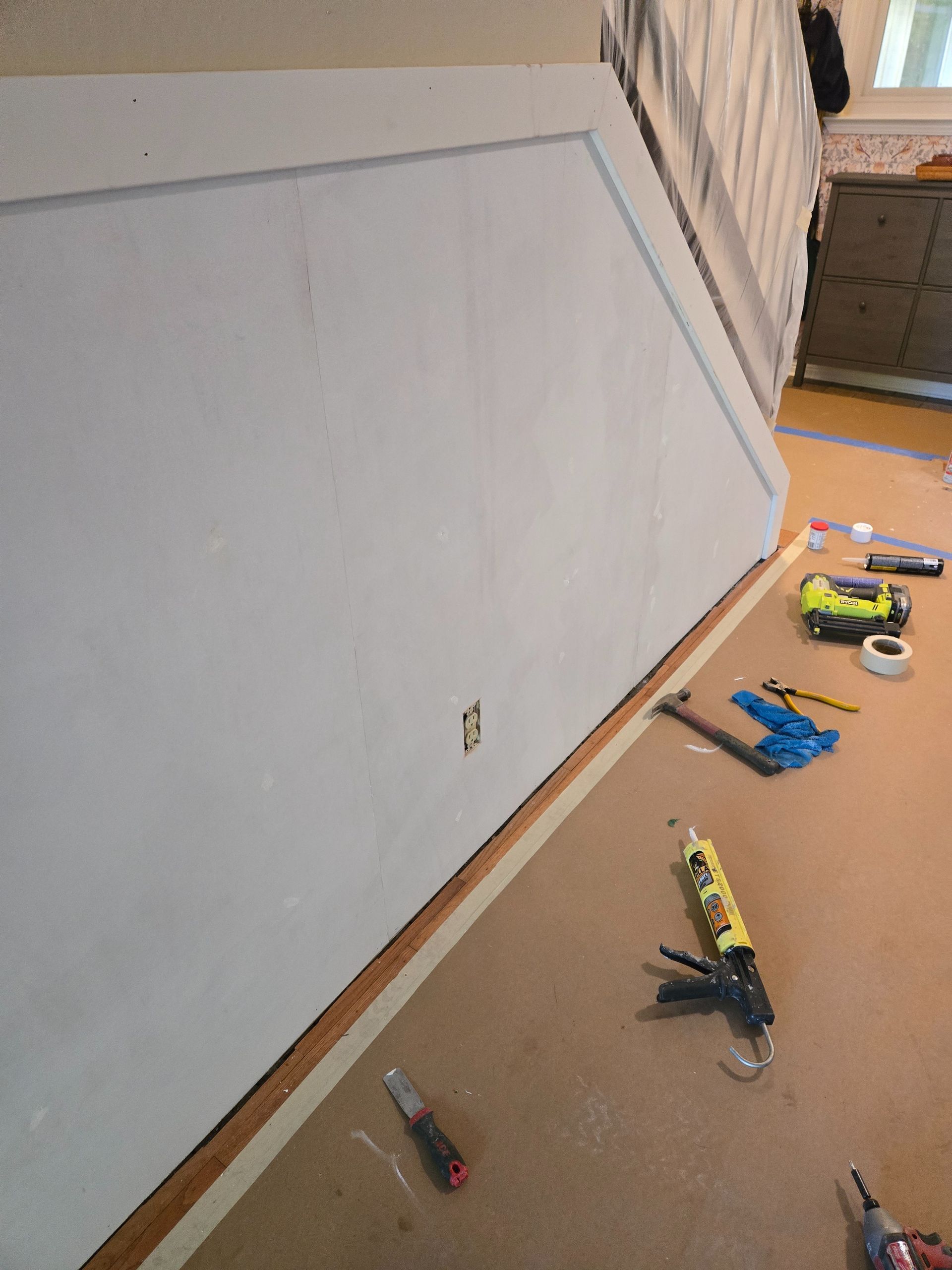 White painted wall with wood trim, tools on floor, tape line. Interior shot.