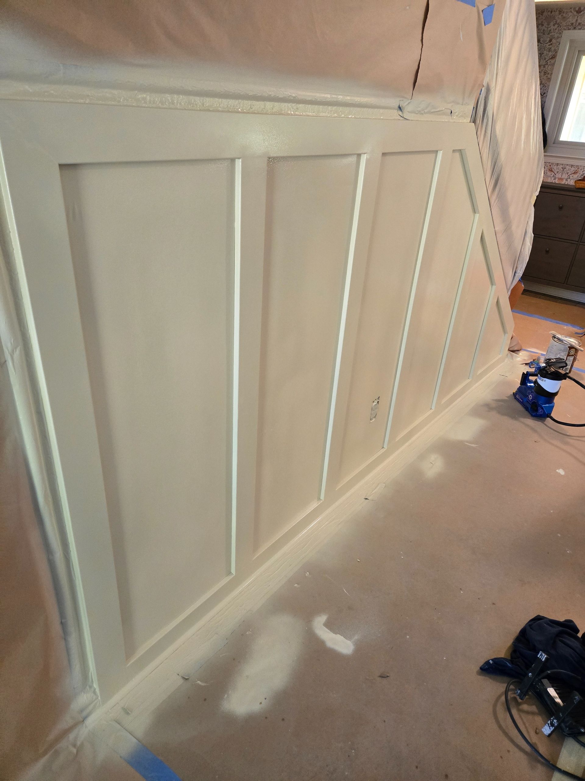 Painted wall paneling in off-white, with vertical and angled sections, spray equipment in the background.