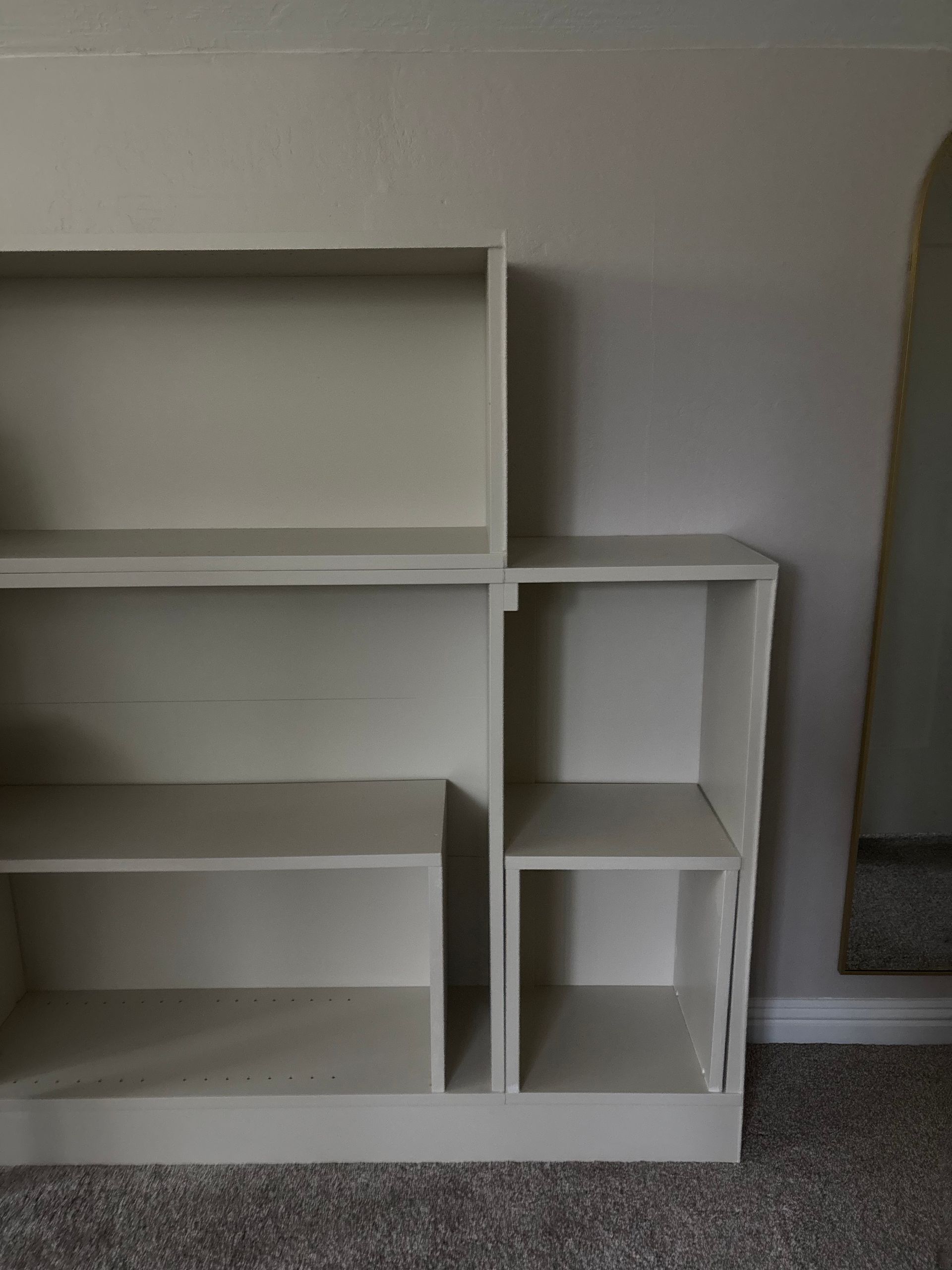 White bookshelf with multiple compartments against a beige wall and carpet.
