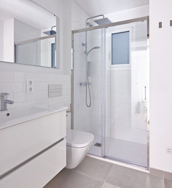 Modern white bathroom with shower, toilet, and vanity, all white with silver fixtures.