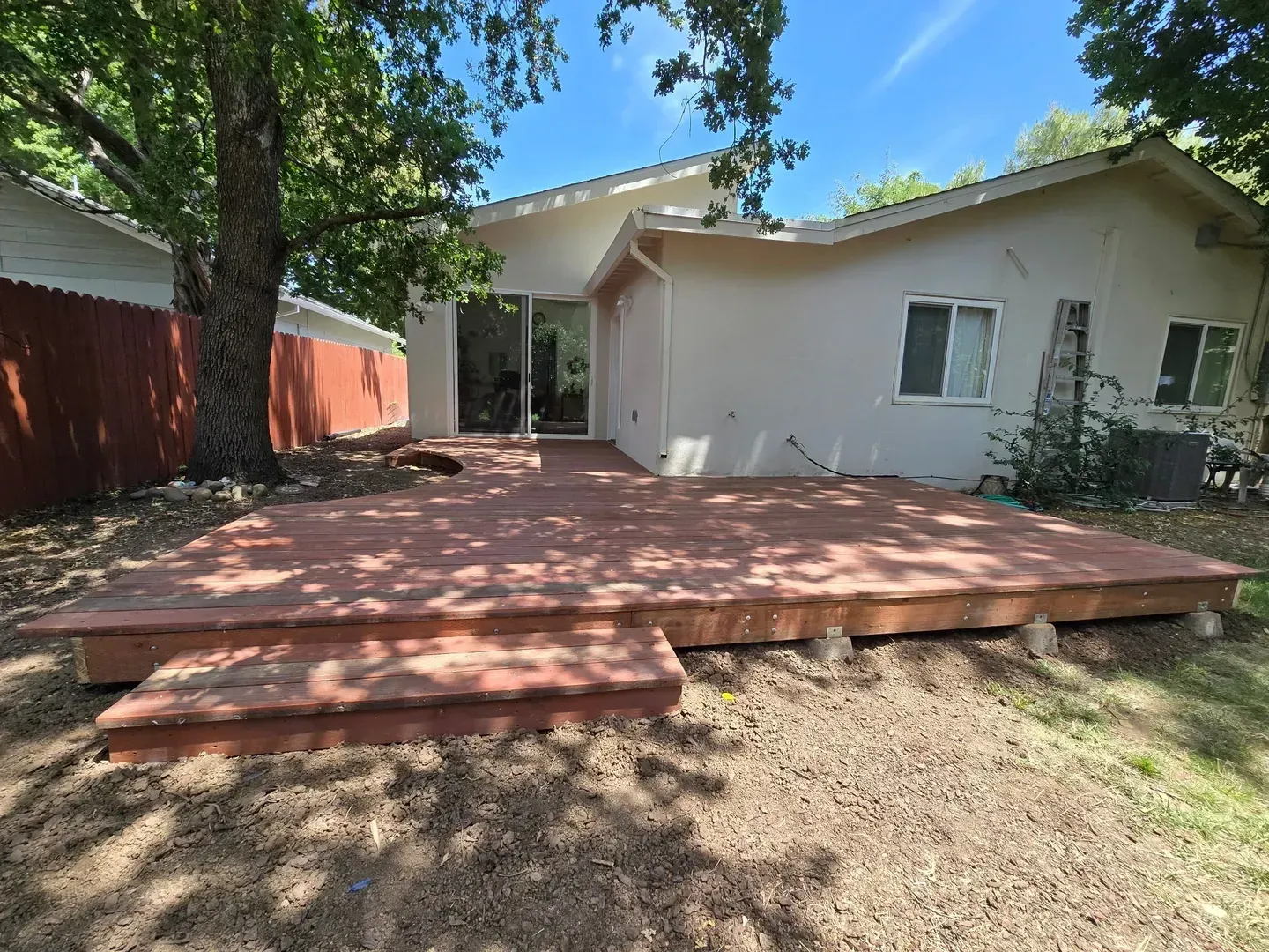 Backyard deck with steps, facing a beige house with a sliding glass door. Reddish-brown wood.
