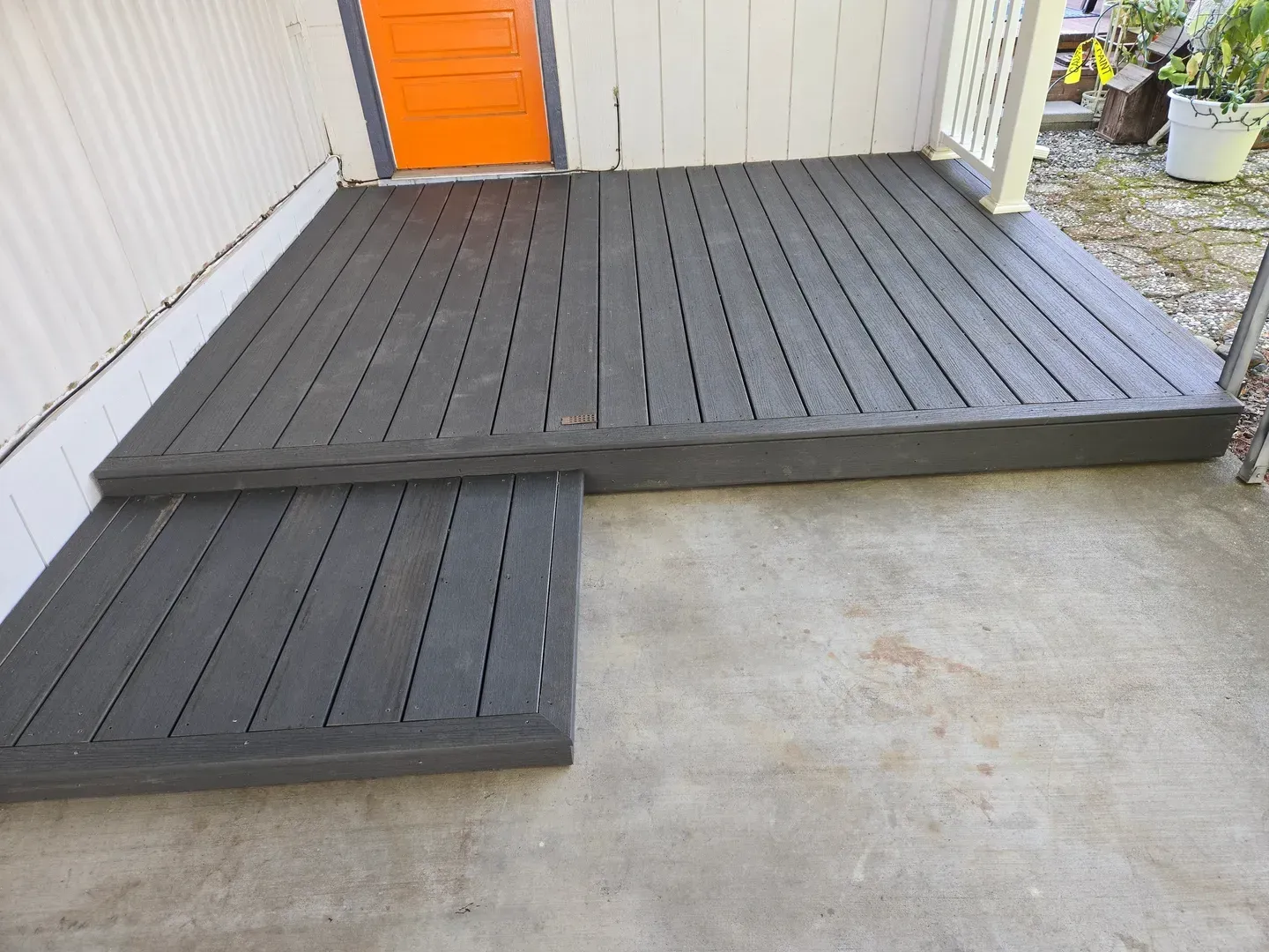 Gray wooden deck with steps leading to an orange door, on a concrete patio.
