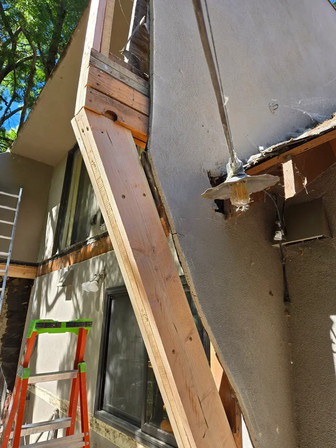 Exterior building construction; exposed wood framing and stucco wall. Ladder visible.