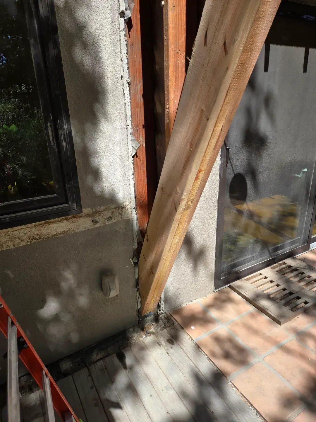 Wooden beam braced against a building's window and door frame, possibly for structural support.