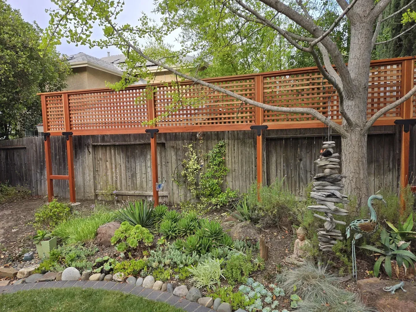 Wooden deck with latticework railing over a weathered wooden fence, garden in front.