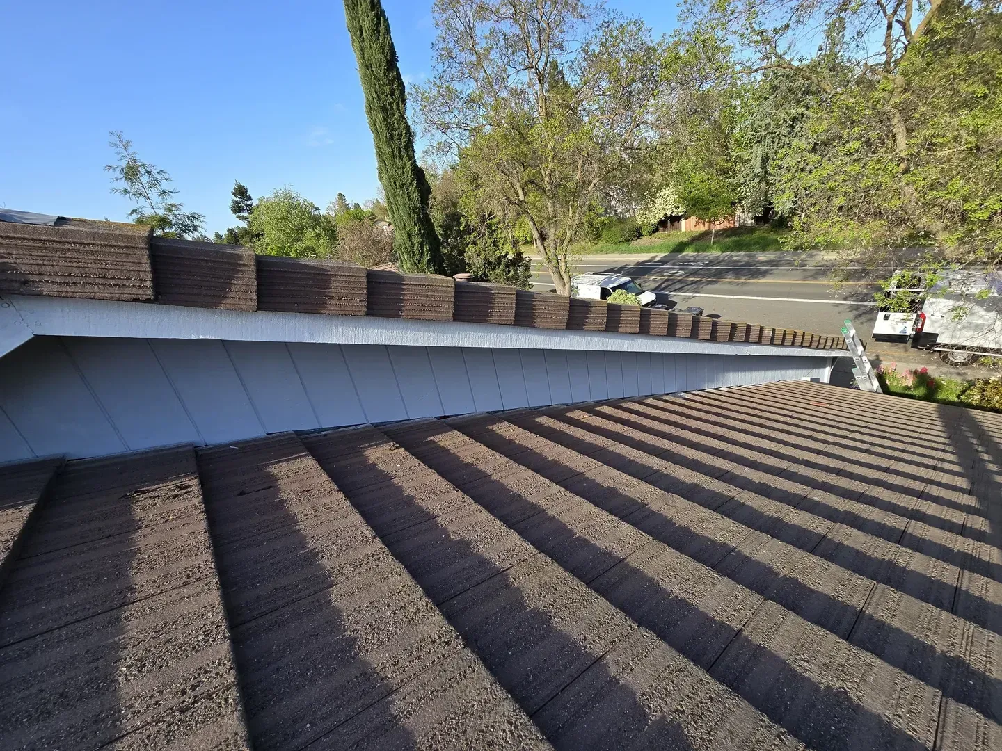 Brown tiled roof with shadow and white trim. Distant trees and road visible.