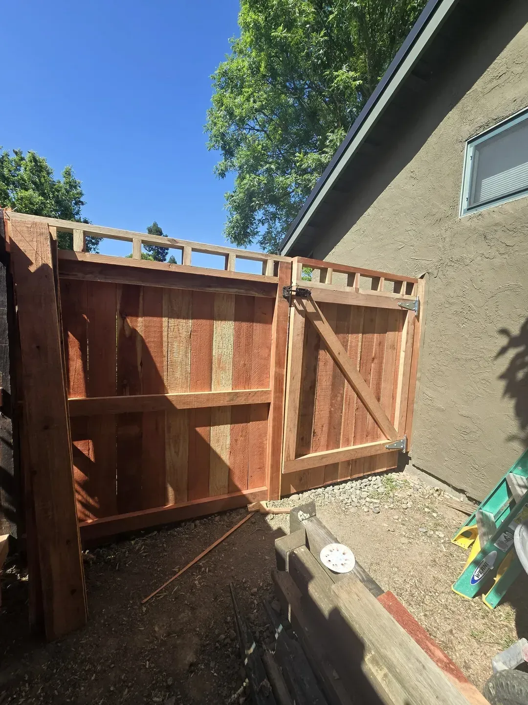 Wooden gate, part of a fence, is open. Adjacent to a stucco wall, in outdoor setting.