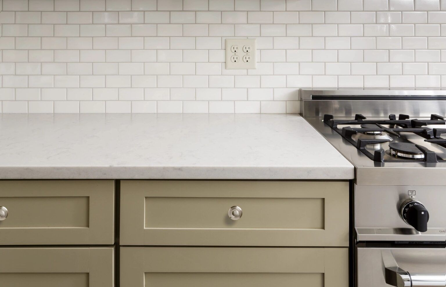 Kitchen with green cabinets, white backsplash, light countertop, and stainless steel range.
