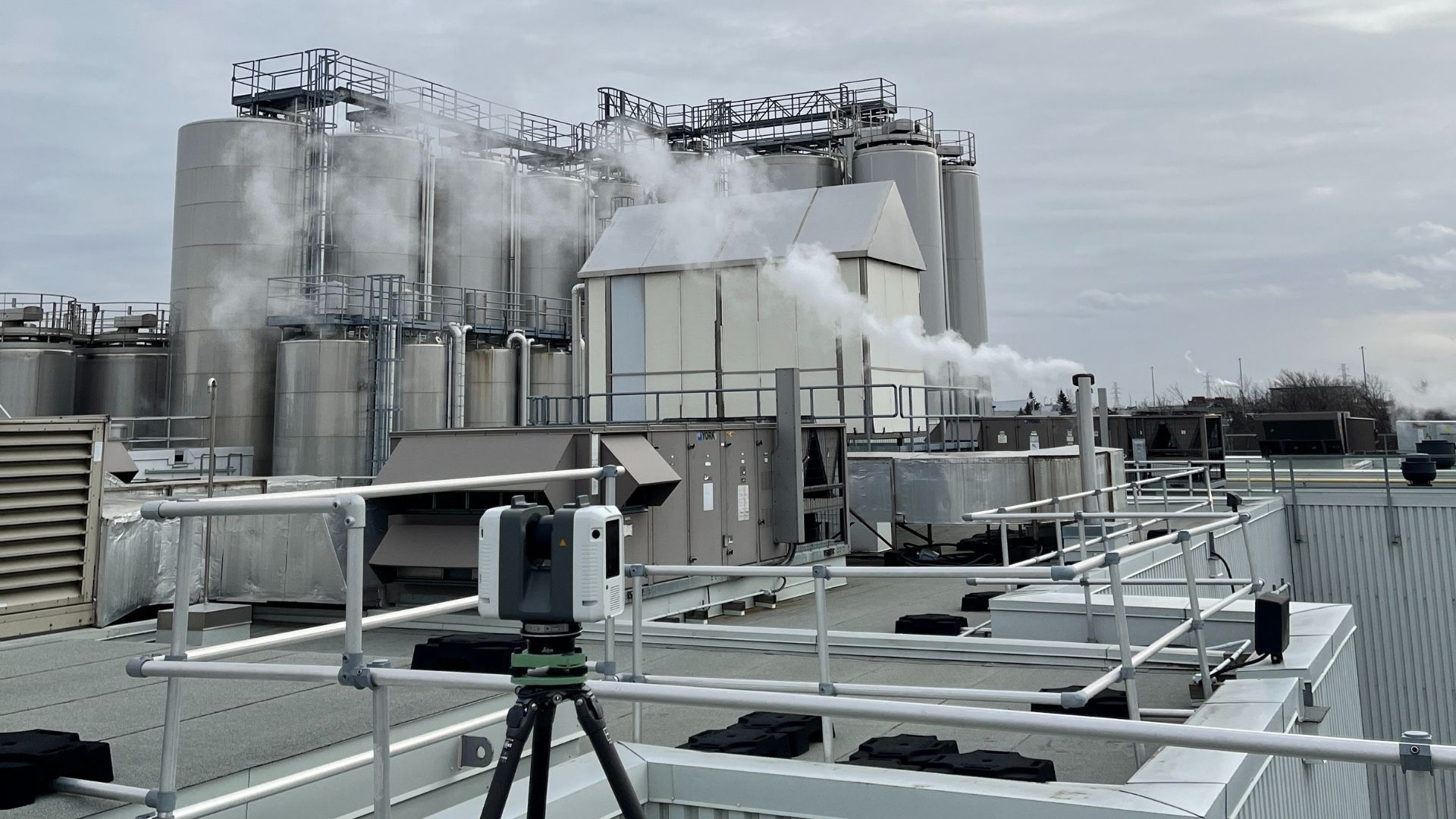 A city street scene with a 3D scanner on a tripod in the foreground; cars and buildings in the background.
